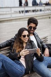 Spain, Barcelona, happy young couple with cell phone resting on a bench - MAUF01556