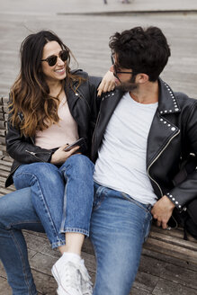 Glückliches junges Paar mit Handy auf einer Bank liegend - MAUF01558