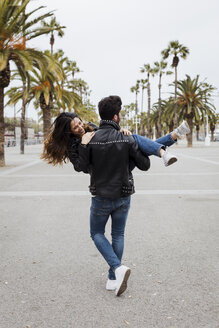 Spanien, Barcelona, junger Mann trägt glückliche Freundin auf Promenade mit Palmen - MAUF01562