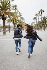 Spain, Barcelona, happy young couple running on promenade with palms - MAUF01564