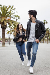 Spanien, Barcelona, glückliches junges Paar läuft auf Promenade mit Palmen - MAUF01565