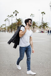 Spain, Barcelona, young man walking on promenade with palms - MAUF01576