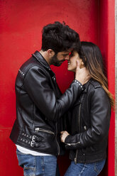 Affectionate young couple kissing at red door - MAUF01580