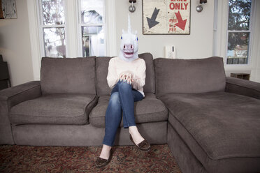 Girl sitting on sofa wearing unicorn head mask - ISF18645