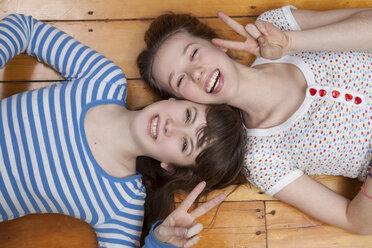 Girls lying on wooden floor doing peace signs - ISF18655