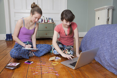Mädchen sitzen mit Laptop auf dem Schlafzimmerboden und machen Freundschaftsarmbänder - ISF18656