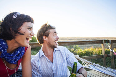 Junges Paar sitzt auf sonnigem Balkon und lächelt - ISF18727
