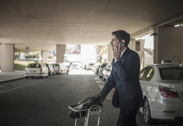 Junger Mann am Handy mit Gepäckwagen im Flughafen - ISF18746