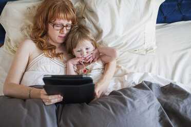 Mutter und Tochter liegen im Bett und schauen auf ein digitales Tablet - ISF18753