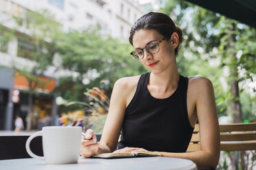 Junge Frau, die in einem Café sitzt, Brainstorming betreibt und Notizen in ein Notizbuch schreibt - KKAF01258