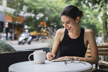 Young woman sitting in coffee shop, brainstorming, writing notes in notebook - KKAF01260