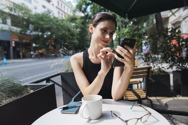 Junge Frau sitzt in einem Kaffeehaus und benutzt ihr Smartphone - KKAF01266