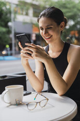 Junge Frau sitzt in einem Kaffeehaus und benutzt ihr Smartphone - KKAF01268