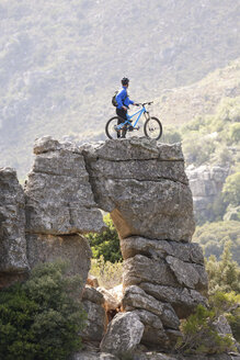 Junger Mann steht mit Mountainbike auf einer Felsformation - ISF18767