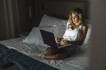 Woman sitting on bed, using laptop - KKAF01323
