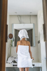 In Handtücher eingewickelte Frau schaut in den Badezimmerspiegel - KKAF01326