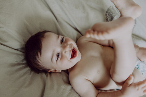 Glückliches Baby, auf dem Bett liegend, lachend - JLOF00104