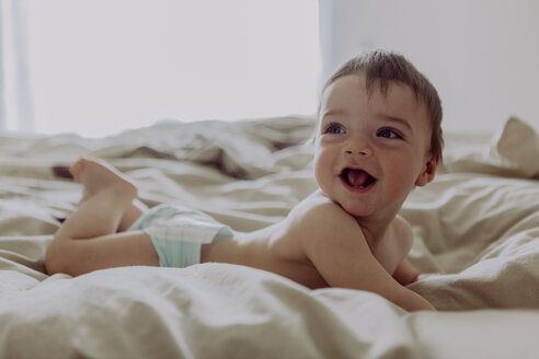 Glückliches Baby, auf dem Bett liegend, lachend - JLOF00109