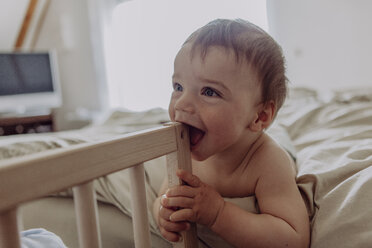 Laughing baby lying on bed, biting his cot - JLOF00110