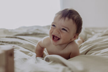 Glückliches Baby, auf dem Bett liegend, lachend - JLOF00111