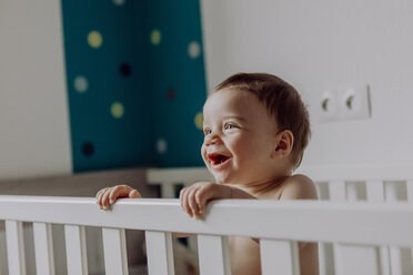 Baby boy standing in his cot, laughing - JLOF00138