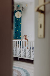 Baby boy standing in his cot, laughing - JLOF00141