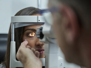 Optometrist examining young woman's eye, contact lens on index finger - CVF01035