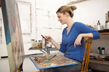 Mittlere erwachsene Frau, die im Atelier eines Künstlers ein Mobiltelefon benutzt - ISF18796