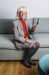 Senior woman sitting on sofa holding mobile phone - ISF18933