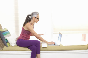 Frau sitzt auf einem Fensterplatz und benutzt einen Laptop - ISF18956