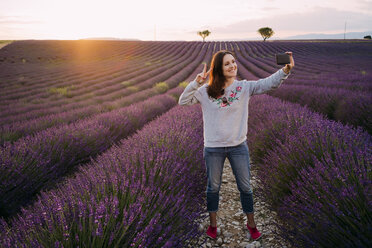 Frankreich, Valensole, lächelnde Frau macht Selfie auf Lavendelfeld bei Sonnenuntergang - GEMF02224
