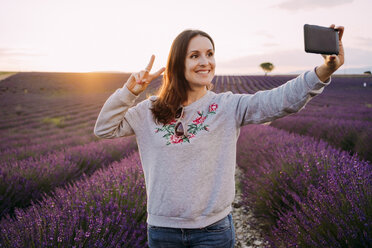 Frankreich, Valensole, Porträt einer lächelnden Frau, die ein Selfie vor einem Lavendelfeld bei Sonnenuntergang macht - GEMF02225