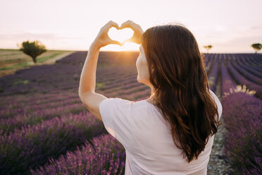 France, Valensole, back view of woman shaping heart with her hands in front of lavender field at sunset - GEMF02229