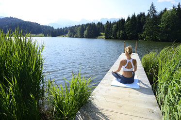 Deutschland, Mittenwald, Rückenansicht einer Frau, die auf einem Steg am See Yoga übt - ECPF00232