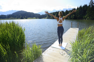 Deutschland, Mittenwald, Rückenansicht einer Frau, die auf einem Steg am See Yoga übt - ECPF00235