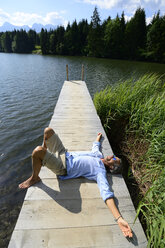 Deutschland, Mittenwald, reifer Mann liegt auf Steg am See und entspannt sich - ECPF00236