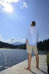 Germany, Mittenwald, back view of mature man standing barefoot on jetty at lake relaxing - ECPF00239