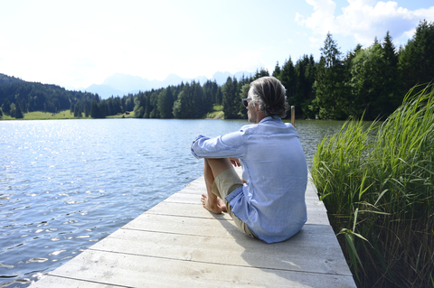 Germany, Mittenwald, mature man relaxing on jetty at lake stock photo