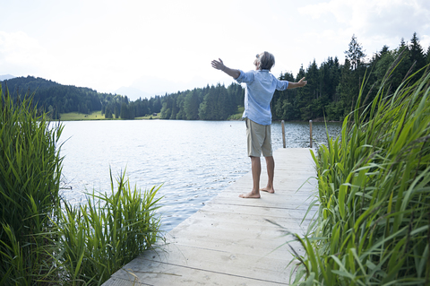 Deutschland, Mittenwald, reifer Mann mit ausgestreckten Armen auf Steg am See stehend, lizenzfreies Stockfoto