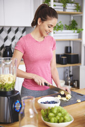 Smiling young woman preparing smoothie in the kitchen - ABIF00779
