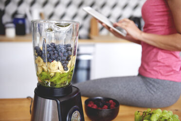 Young woman using tablet in the kitchen while preparing smoothie - ABIF00785