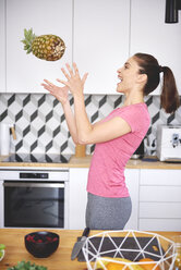 Junge Frau wirft in der Küche Ananas in die Luft - ABIF00788