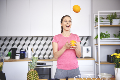 Portrait of young woman juggling with oranges in the kitchen stock photo