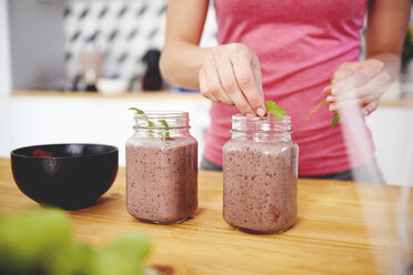 Woman's hand garnishing glass of raspberry smoothie - ABIF00794