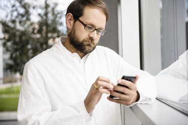 Arzt benutzt Mobiltelefon am Fenster - CUF43685