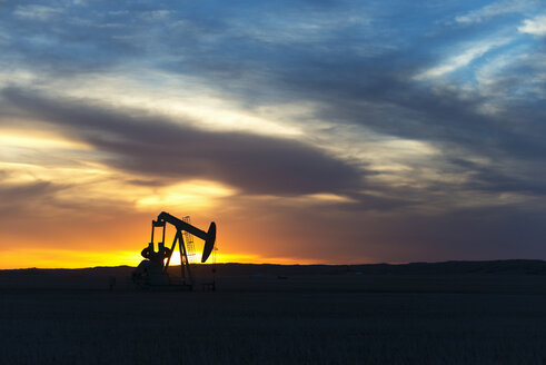 Ein Pumpjack an einer Ölbohrstelle bei Sonnenuntergang. - MINF03037
