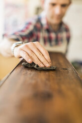 Ein Restaurator für antike Möbel bei der Arbeit, der mit einem Tuch eine glatte Holzoberfläche poliert. - MINF03055