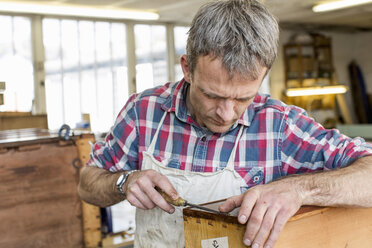 Ein Mann in einer Möbelrestaurierungswerkstatt arbeitet mit einem Handwerkzeug an einem antiken Möbelstück. - MINF03056
