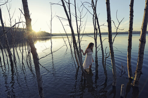 Eine Frau in einem weißen Kleid im flachen Wasser in der Abenddämmerung - MINF03058