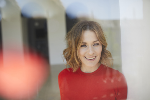 Portrait of smiling woman wearing red shirt looking out of window stock photo